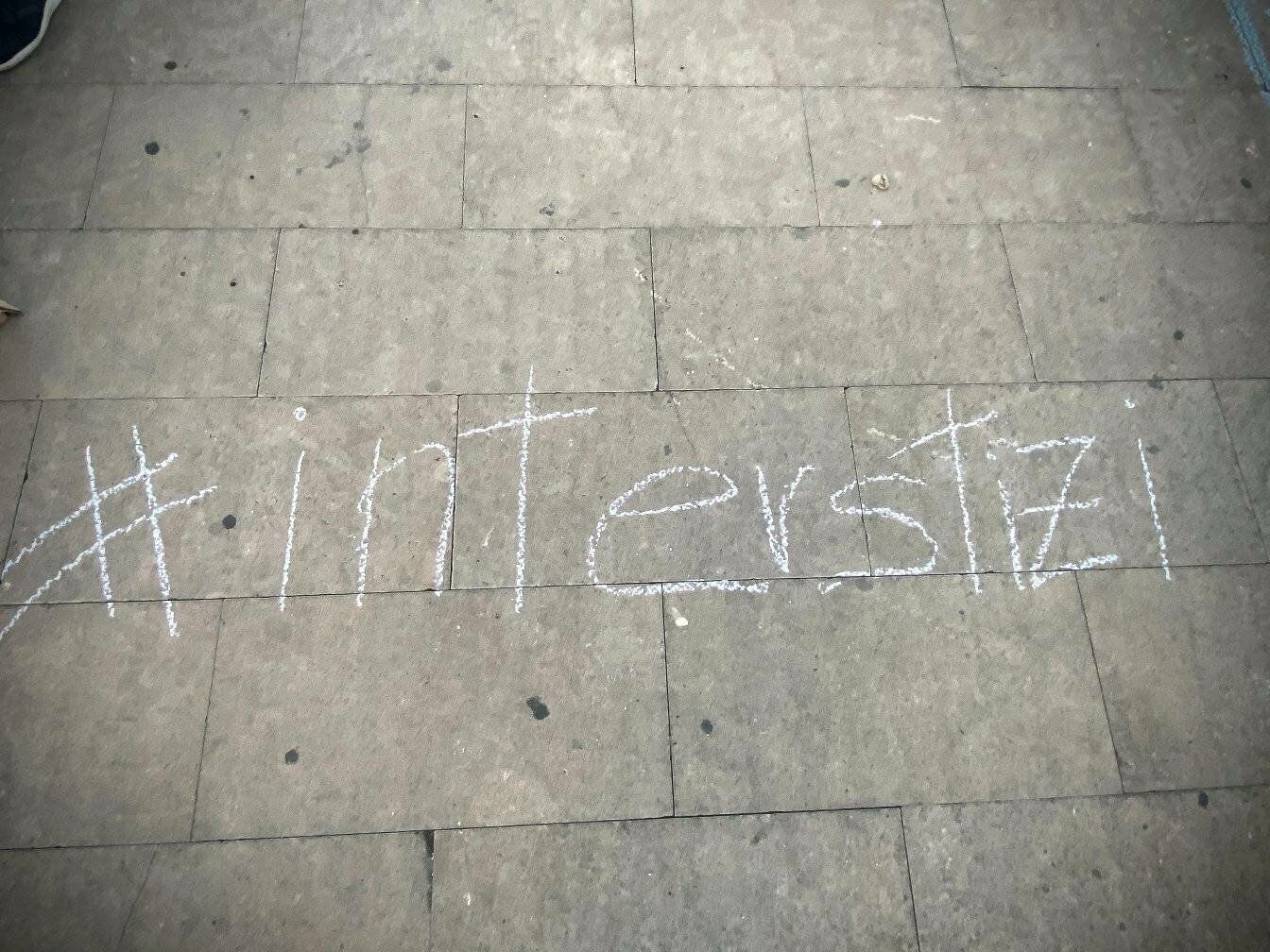 Nome dell'associazione Interstizi scritto su un pavimento con gesso bianco